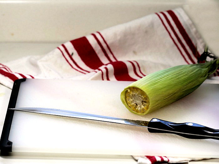 sharp knife and corn ear that has been cooked in the microwave