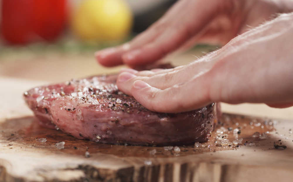 Hands adding rub to steak.