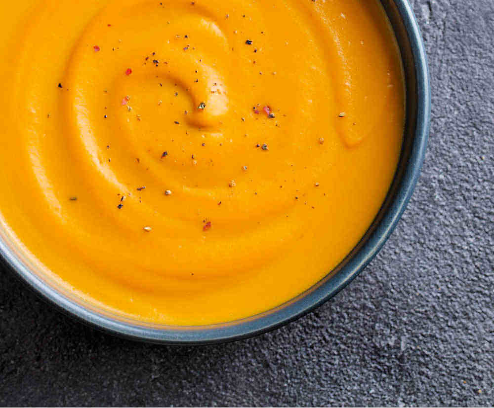 Thick curried carrot soup in a gray bowl.