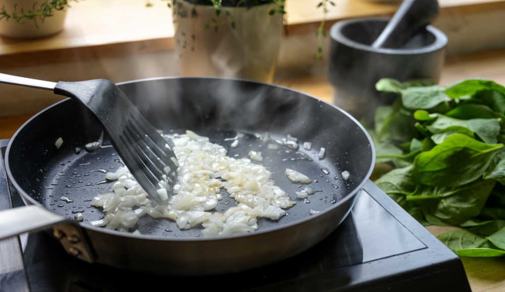 Cooking onions in a pan with Brussels sprouts leaves and herbs.