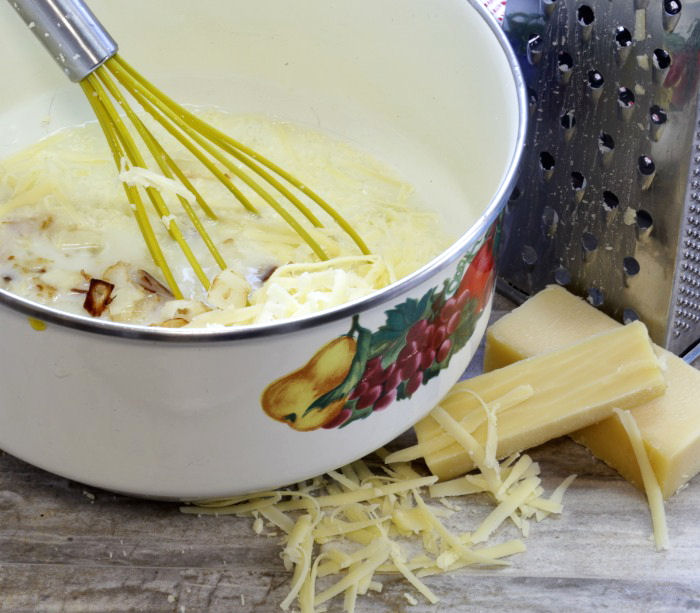 Egg white cheese mixture in a bowl with whisk, near some Gruyere cheese.