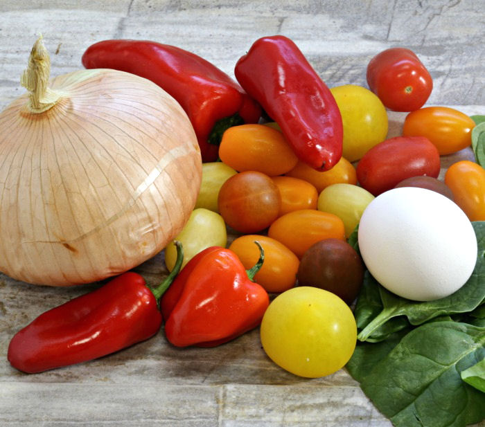 Onions, egg, baby tomatoes, spinach and baby tomatoes on a counter top.