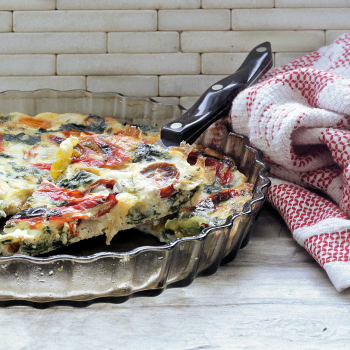 Slice of egg white breakfast quiche being removed from a quiche pan near a red and white towel.