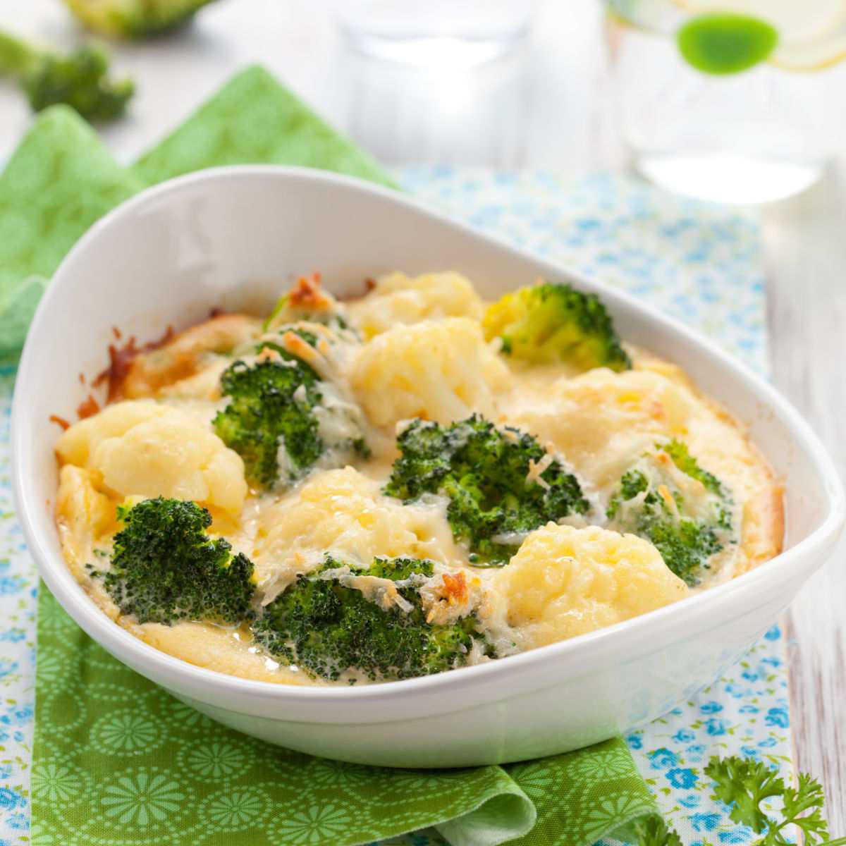 broccoli cauliflower au gratin Broccoli and cauliflower with cheddar cheese in a white dish with a green napkin.