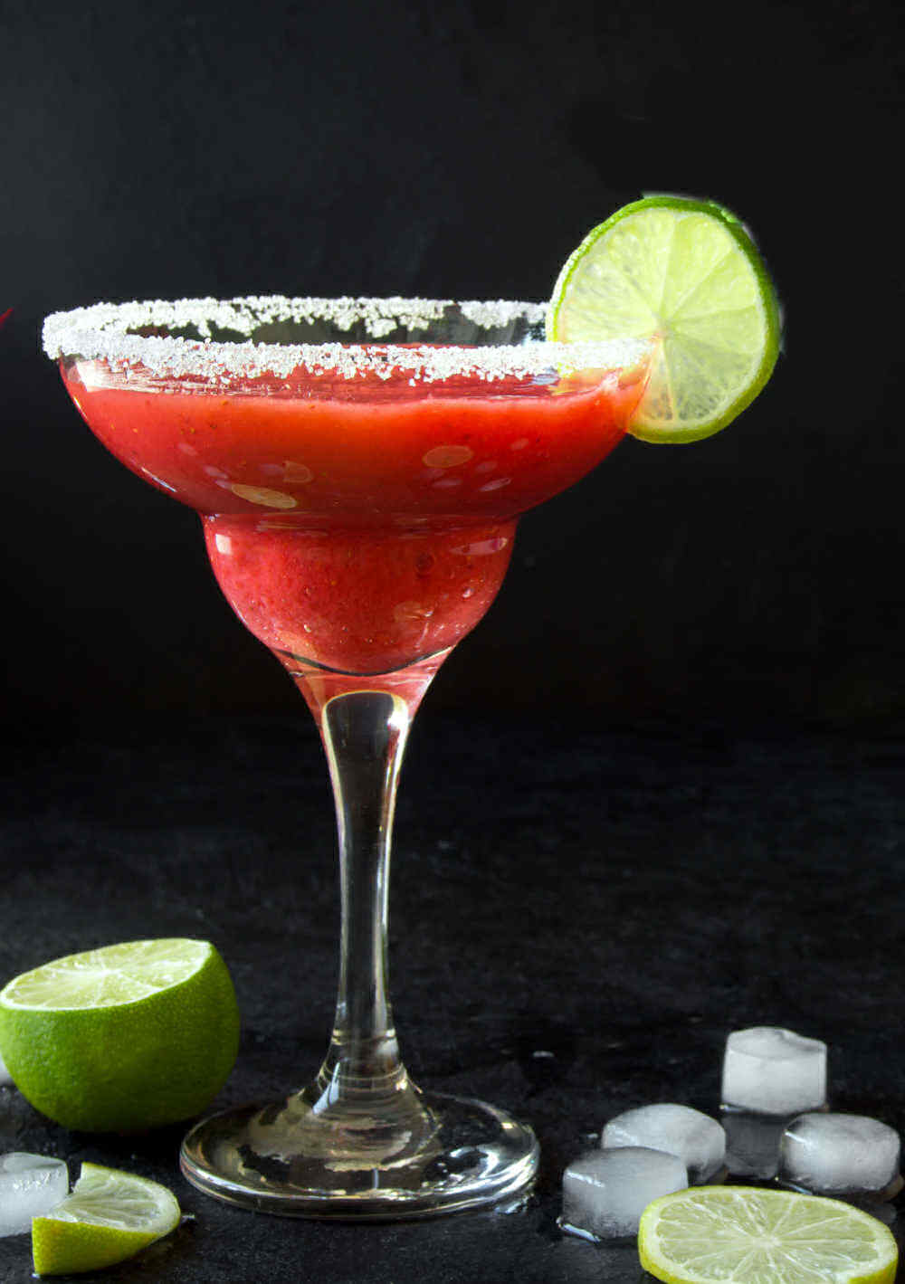 Slushy strawberry drink in a martini glass with salt and lime.