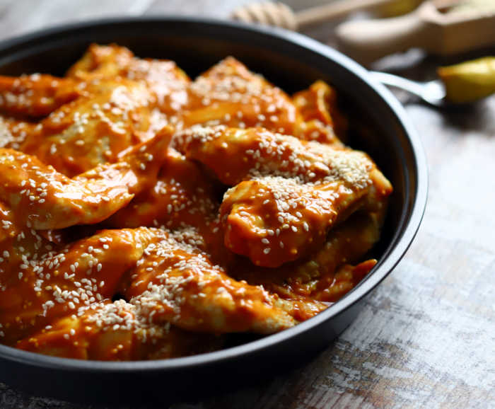 chciken wings marinating in a bowl with sesame seeds.