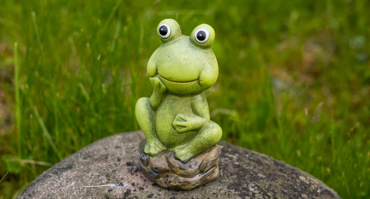 Ceramic frog sitting on a rock in a garden.