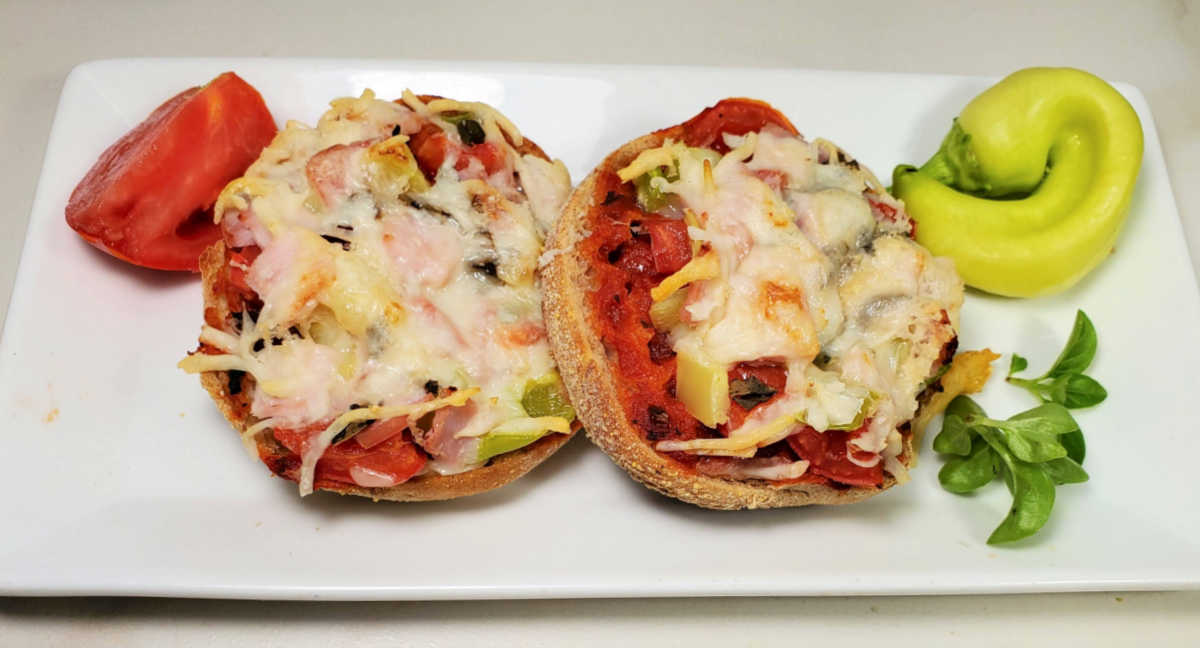 Breakfast pizzas on a white plate with vegetables and fresh basil.