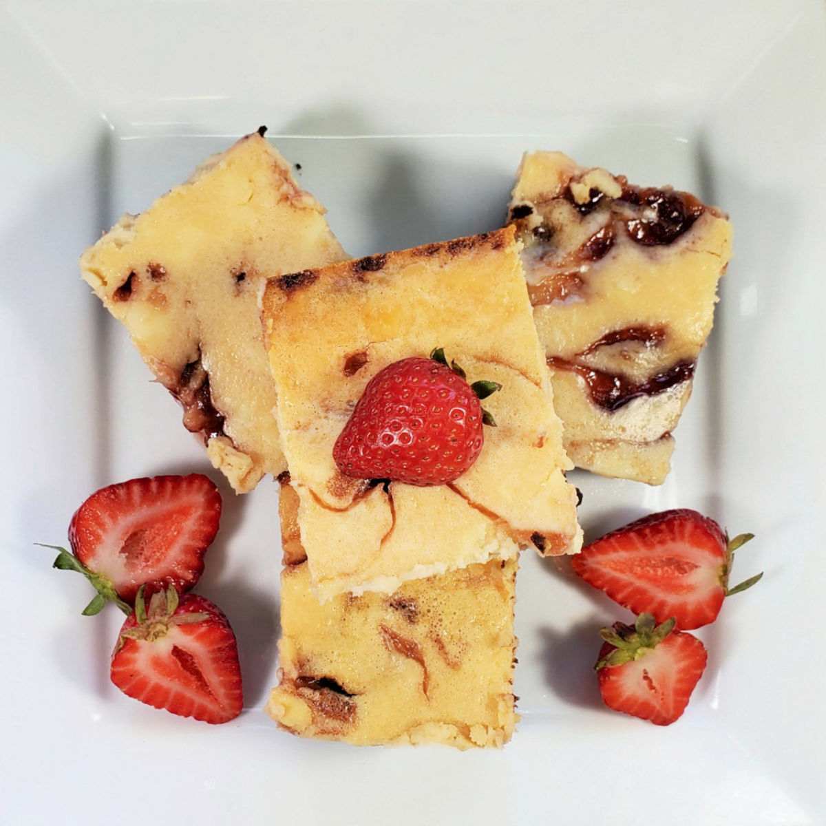 Brownies with cheesecake swirl and sliced strawberries on a white plate.