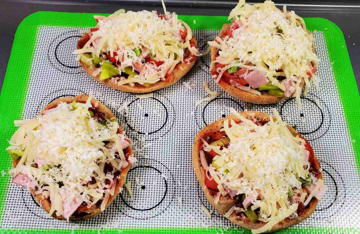 Mini breakfast pizzas on a silicone mat, ready to bake in the oven.