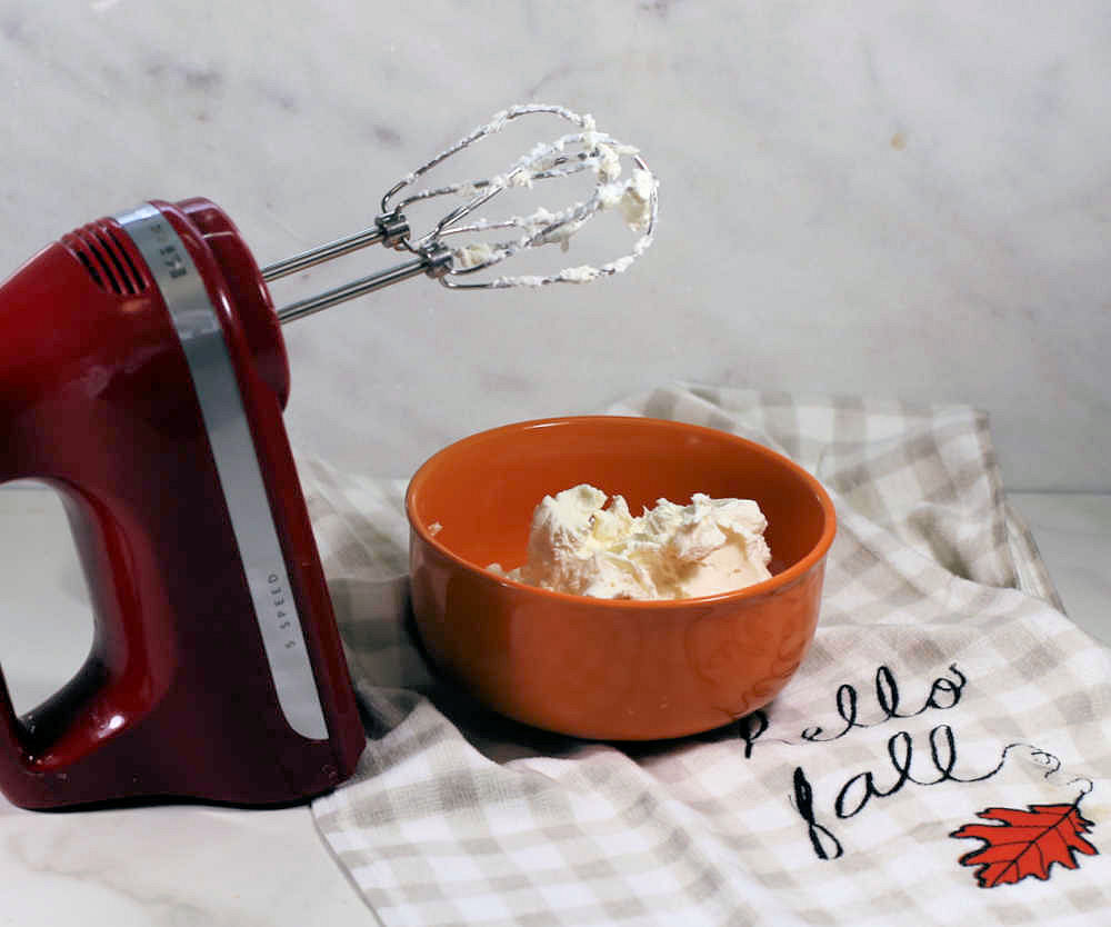 Red mixer with cream cheese in an orange bowl.