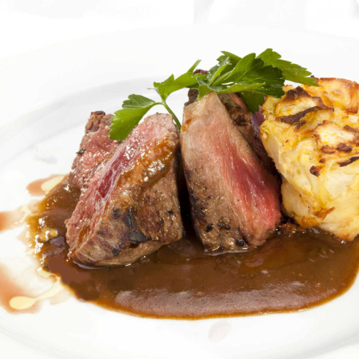 Sirloin steaks with Irish Whiskey sauce and potatoes on a white plate.