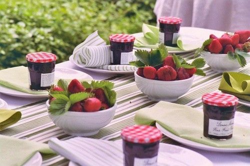 Strawberry themed tablescape with bowls of strawberries and jars of jam.
