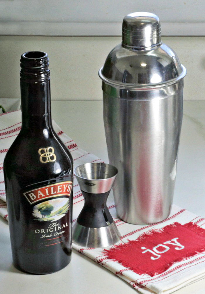 Cocktail shaker and opened bottle of Bailey's Irish Cream near a Joy tea towel.