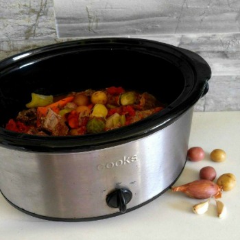 Slow cooker filled with root vegetables and onions.