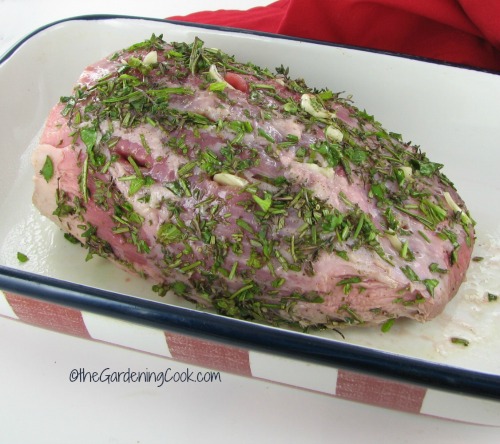 fresh herb coating on a roast of beef in a red and blue pan.