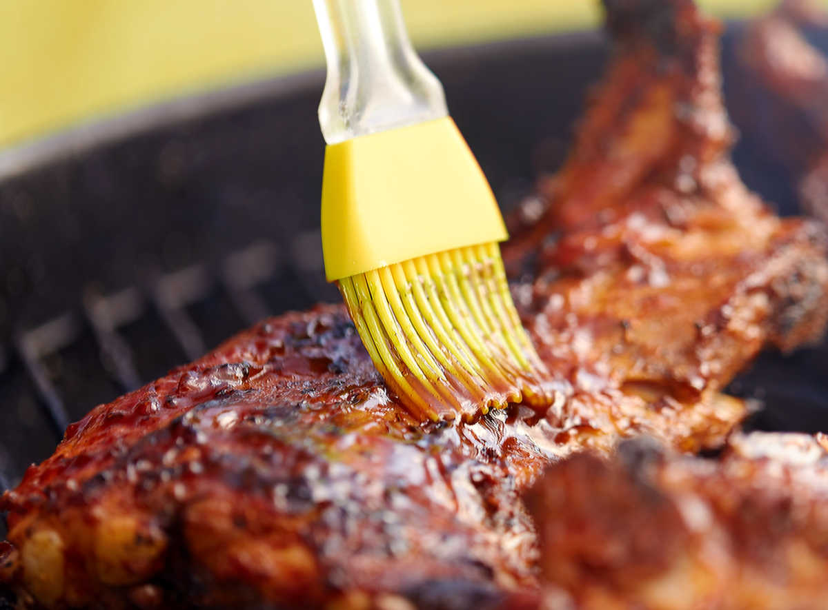Yellow silicone brush adding BBQ sauce to meat.
