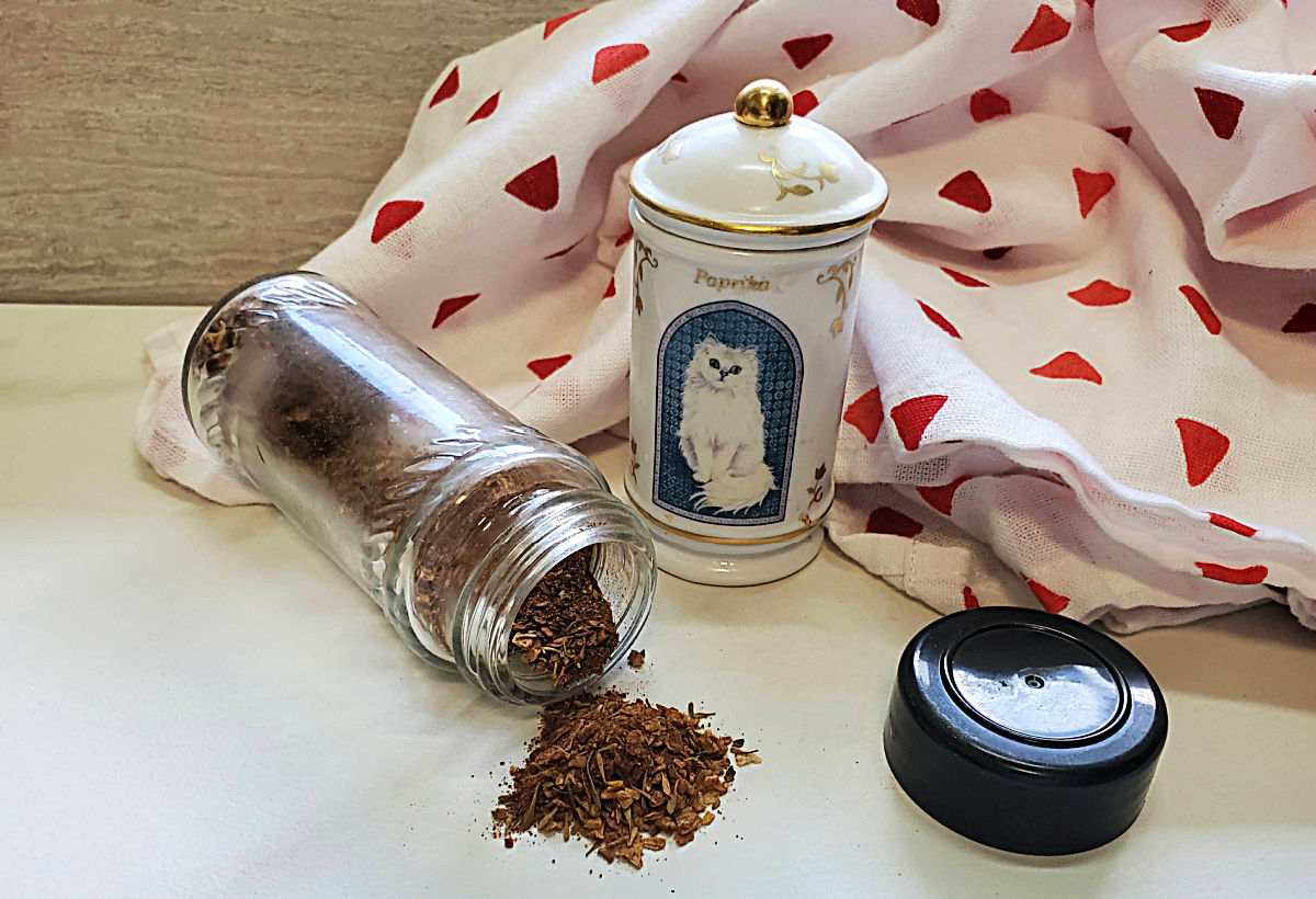 Cat spice jar with paprika and jerk seasoning overturned near a tea towel.