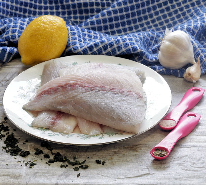Barramundi fillets on a plate with lemon, basil, herbs and garlic.