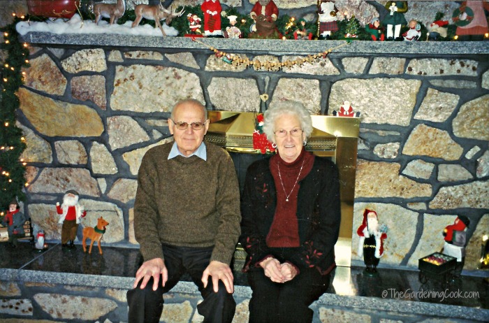 Mum and Dad at Christmas time near a fire hearth with decoration.