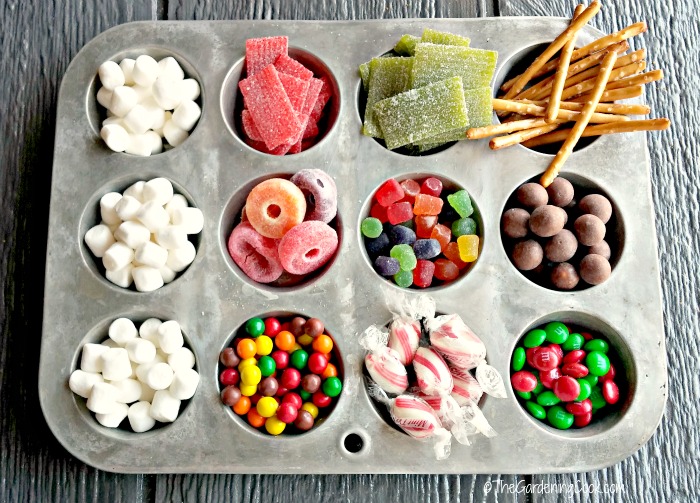 Marshhmallows, striped candy, pretzels, gumdrops and M&Ms in muffin tin for a Gingerbread house.