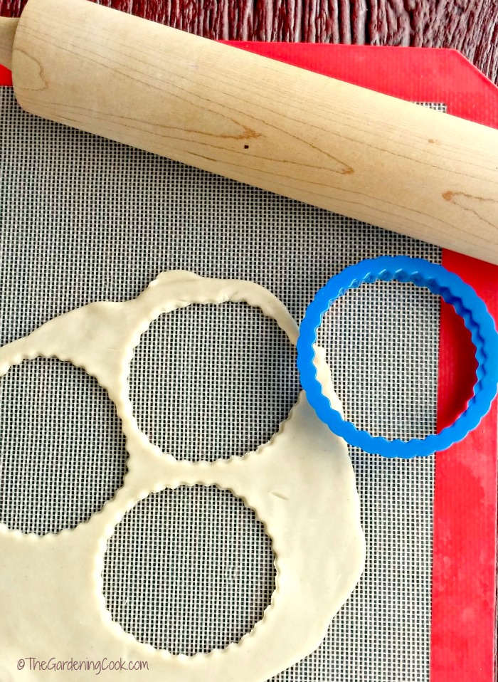 Rolling pin, cookie dough and plastic cookie cutter on a silicone mat.