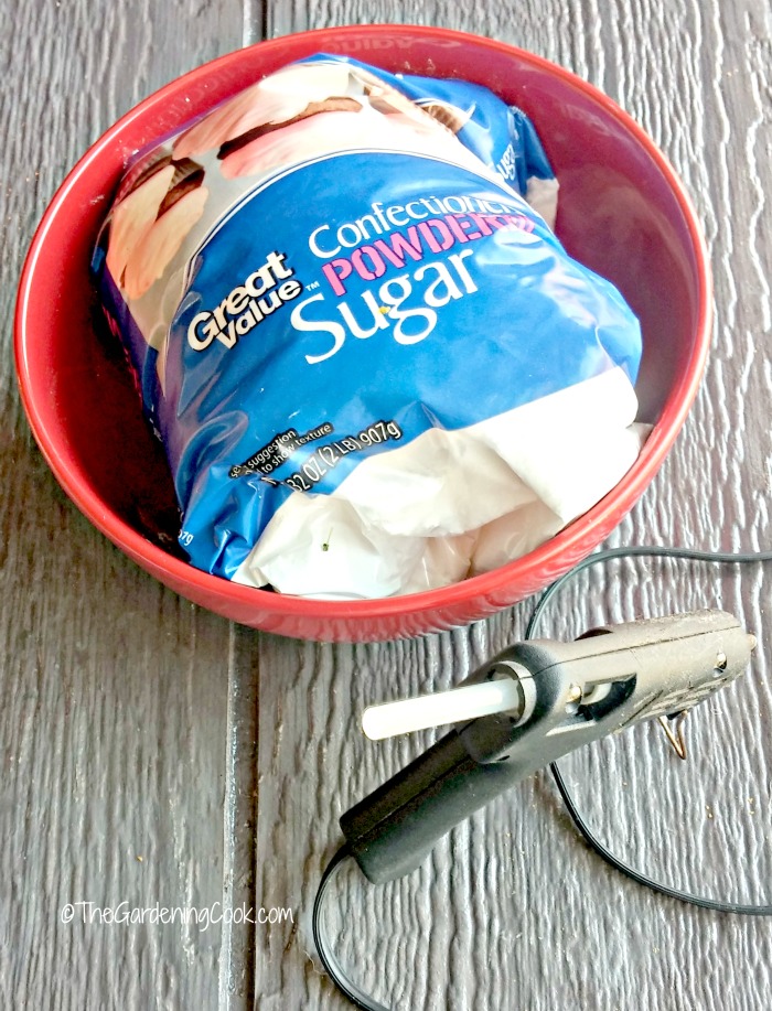Bag of powdered sugar in a red bowl with a hot glue gun. 