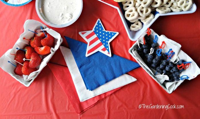 Strawberries, dip, yogurt pretzels and blueberries with flag star and red white and blue napkins.