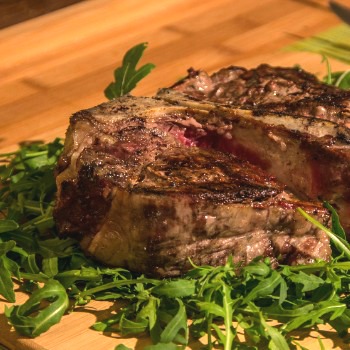 Cooked steak over greens on a cutting board.