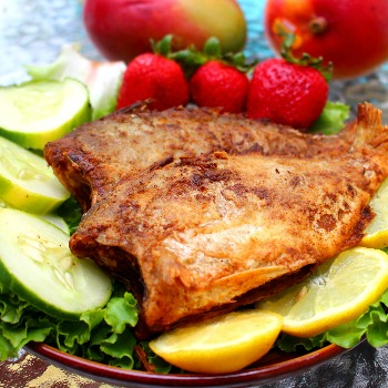 Pan fried fish with fruit and slad on a red plate.