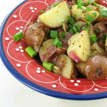 German potato salad recipe with bacon and spring onions in a red bowl.