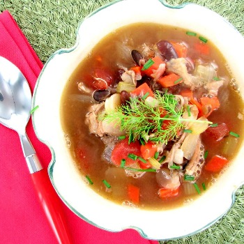 White bowl filled with vegetable soup and red napkin and spoon.
