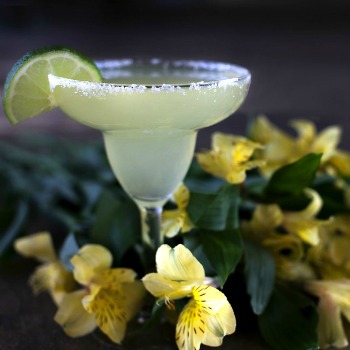 Margarita with salt and lime surrounded by yellow flowers.