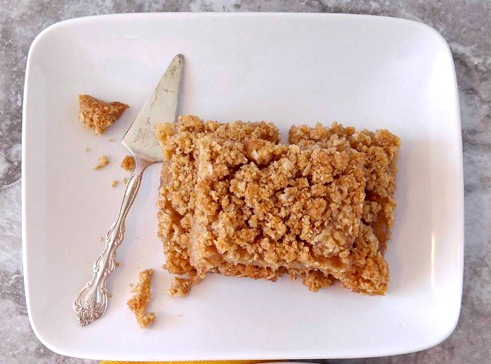 Close up of apple pie bars on a white plate with a serving tool.