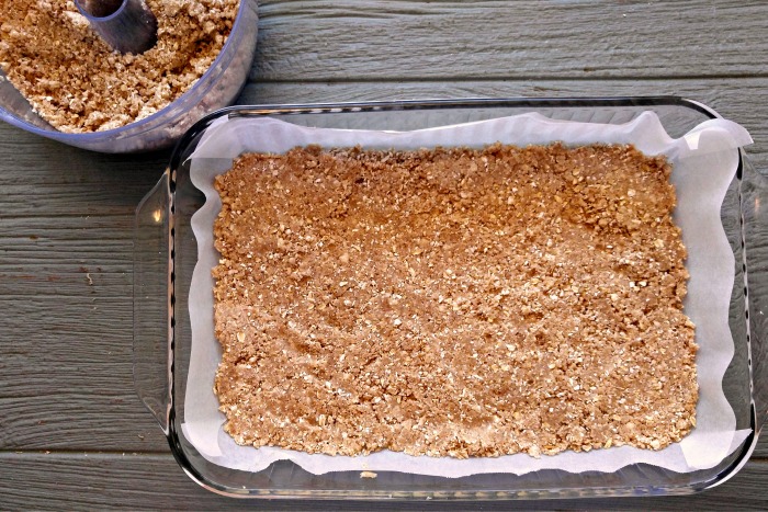 Rolled oat mixture in a pan with ingredients nearby in a food processor.