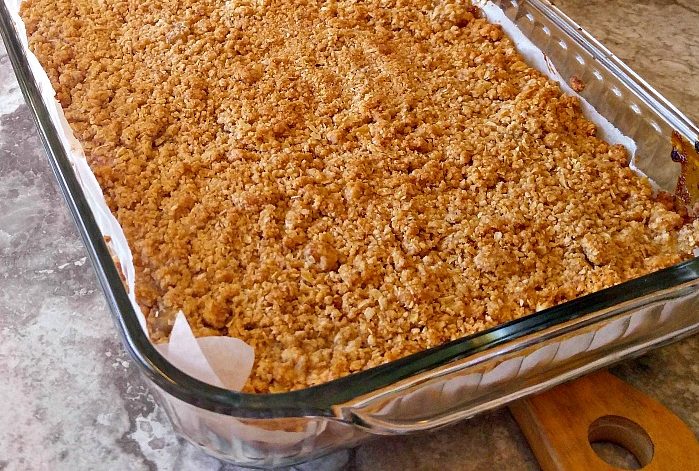 Cooked apple pie oatmeal bars in a glass pan with parchment paper.