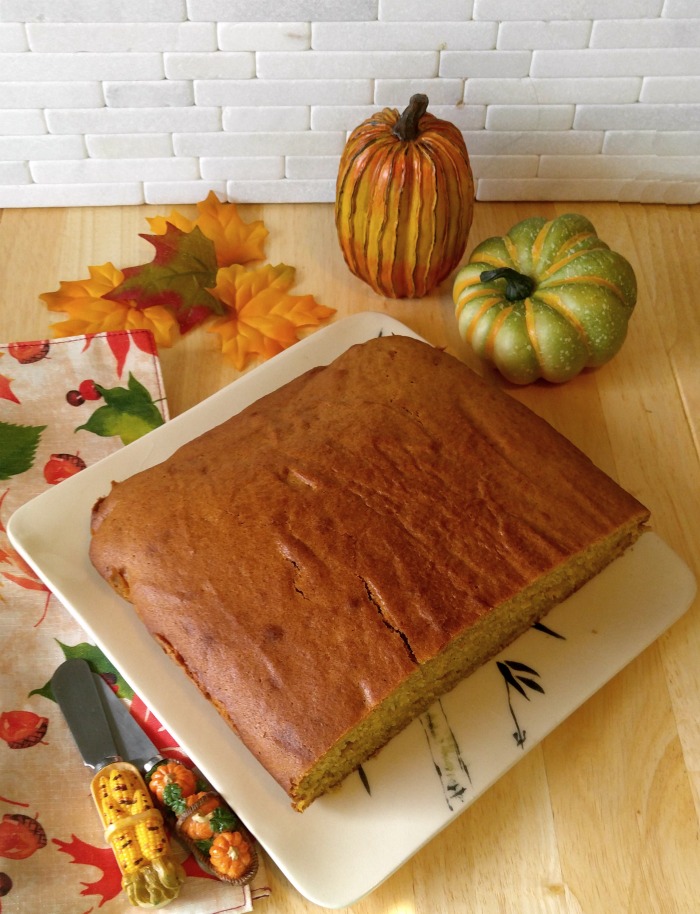 Pumpkins and leaves near a half of a pumpkin spice cake.