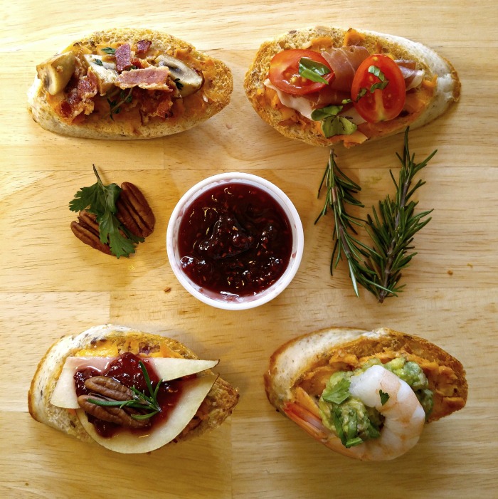 Crostini appetizers on a wood board with rosemary, pecans and sauce.