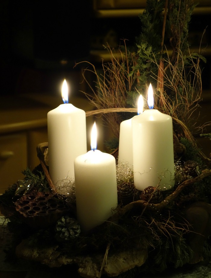 White candles lit in a basket with dried greenery.