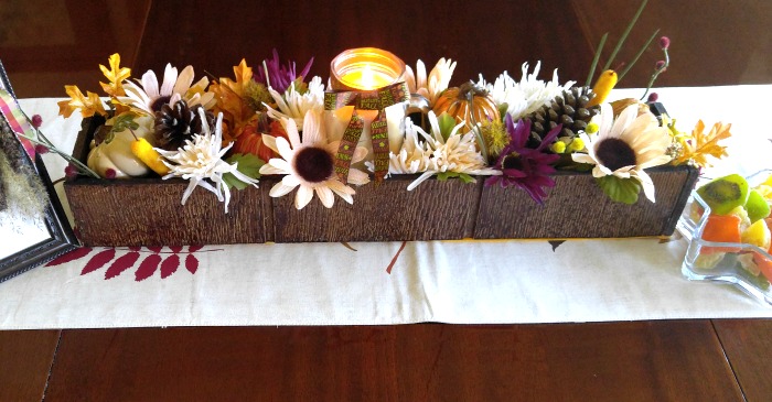 Runner on a wooden table with box filled with flowers.