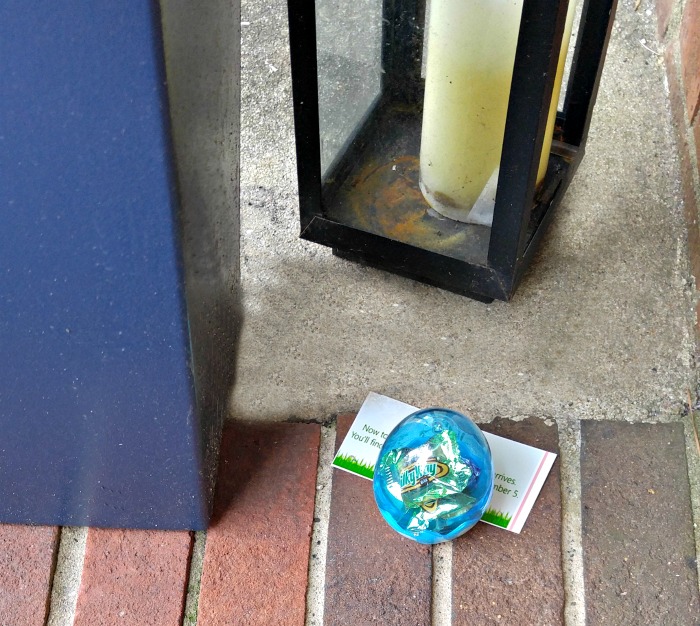 Easter egg and clue near a blue planter and tall candle.