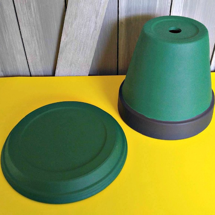 Painted clay pot and saucer on a yellow board near a wooden wall.