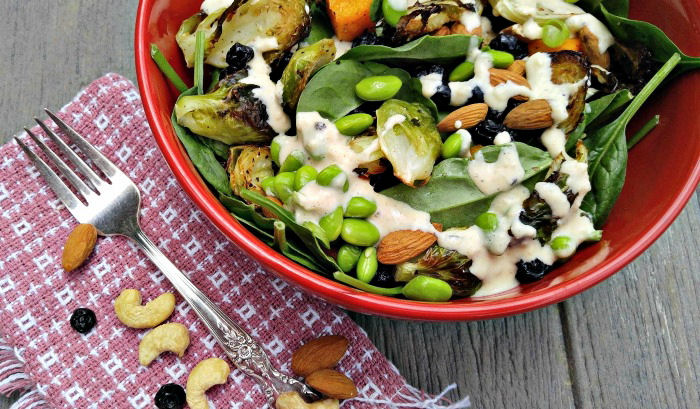 Bowl of roast vegetable salad with fork and nuts.
