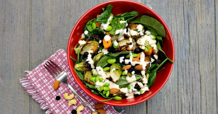 roast vegetable salad in a red bowl with a fork, pink napking and nuts.