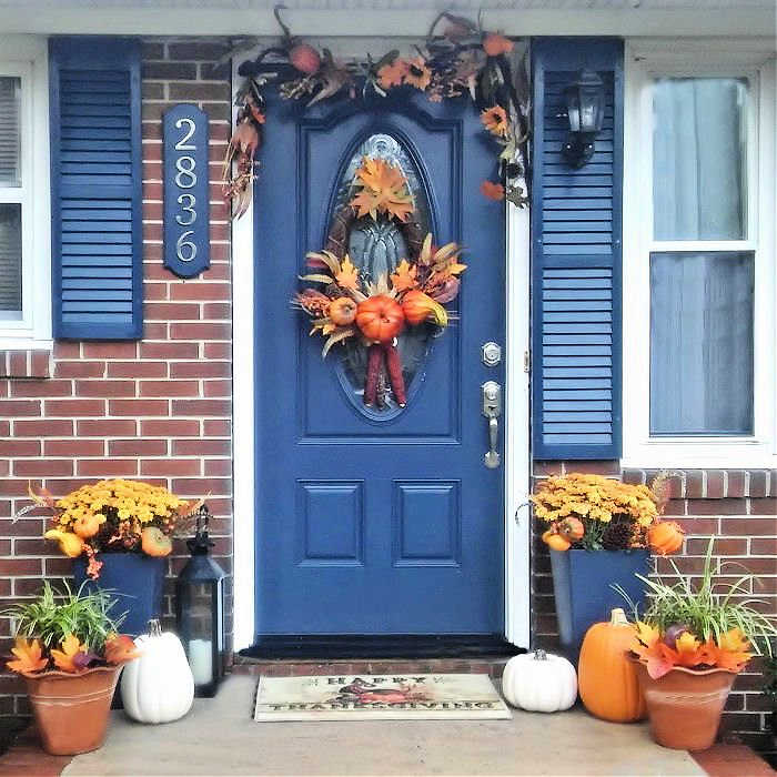 Blue door with greenery for fall and planters in an entryway..