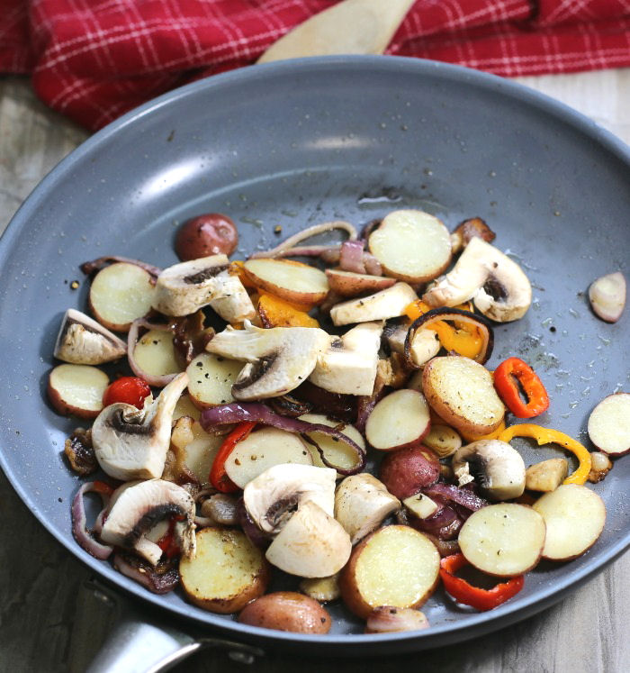 Pan cooking mushrooms, potatoes, peppers and onions