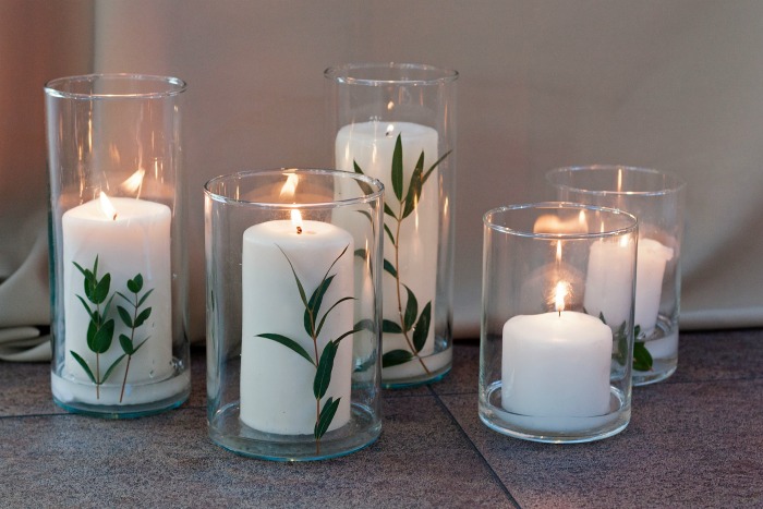 White candles with eucalyptus leaves on holders.