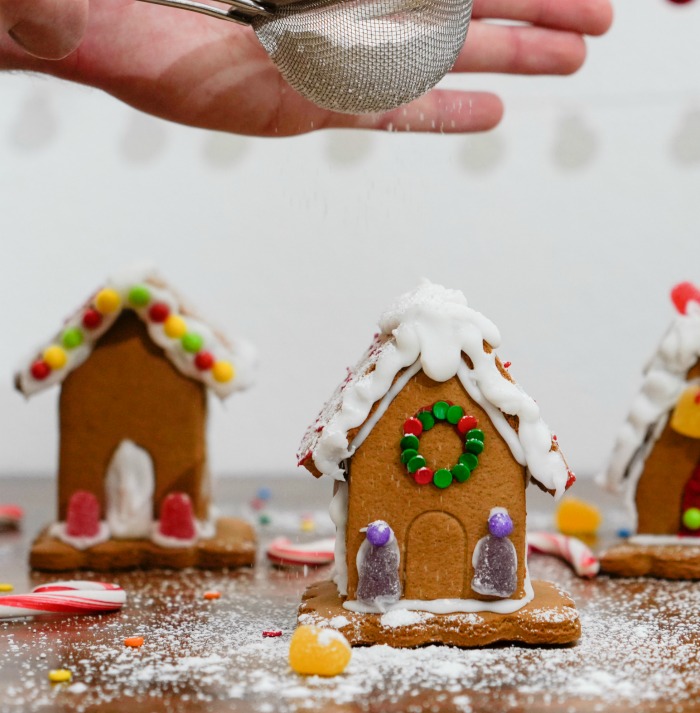 Dusting a gingerbread house with a sifter and sugar.