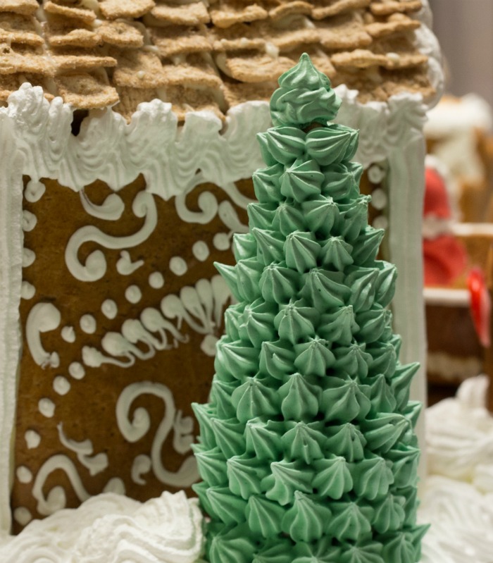 Waffle cone Christmas trees with green frosting near a gingerbread house.