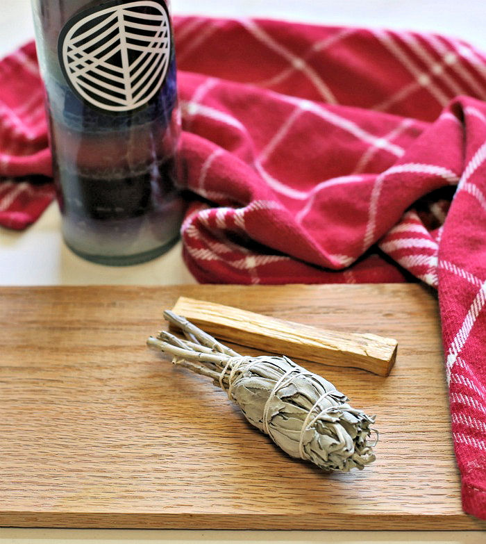 White sage for smudging on a board with a red towel and black candle.